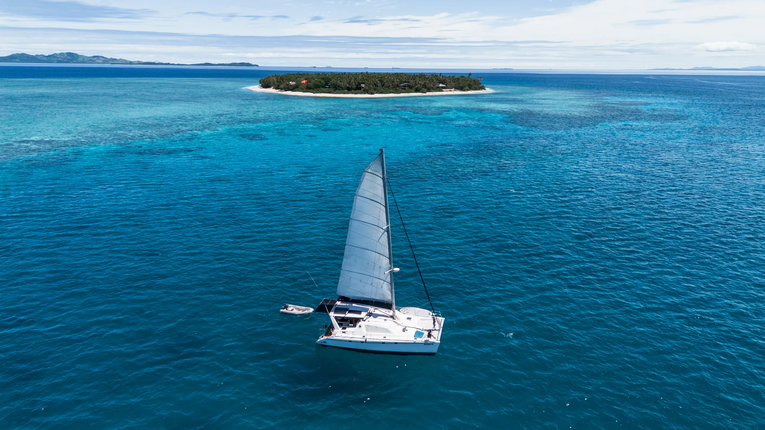 Sailing catamaran on turquoise water beside an island
