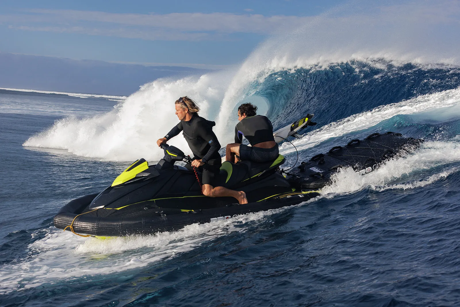 Jet ski and surfers beside a breaking wave